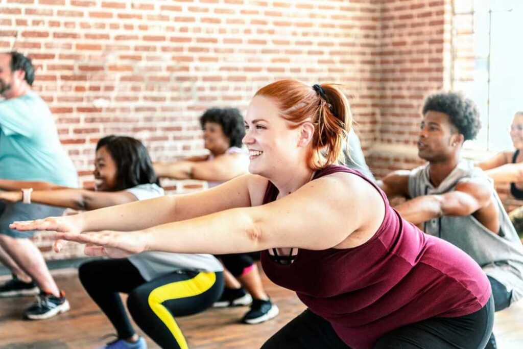 A woman leading a group of people in a gym, demonstrating squats with perfect form and technique.