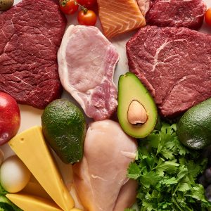 Top view of assorted raw meat, poultry, fish, eggs, vegetables, fruits, nuts, greenery and cheese